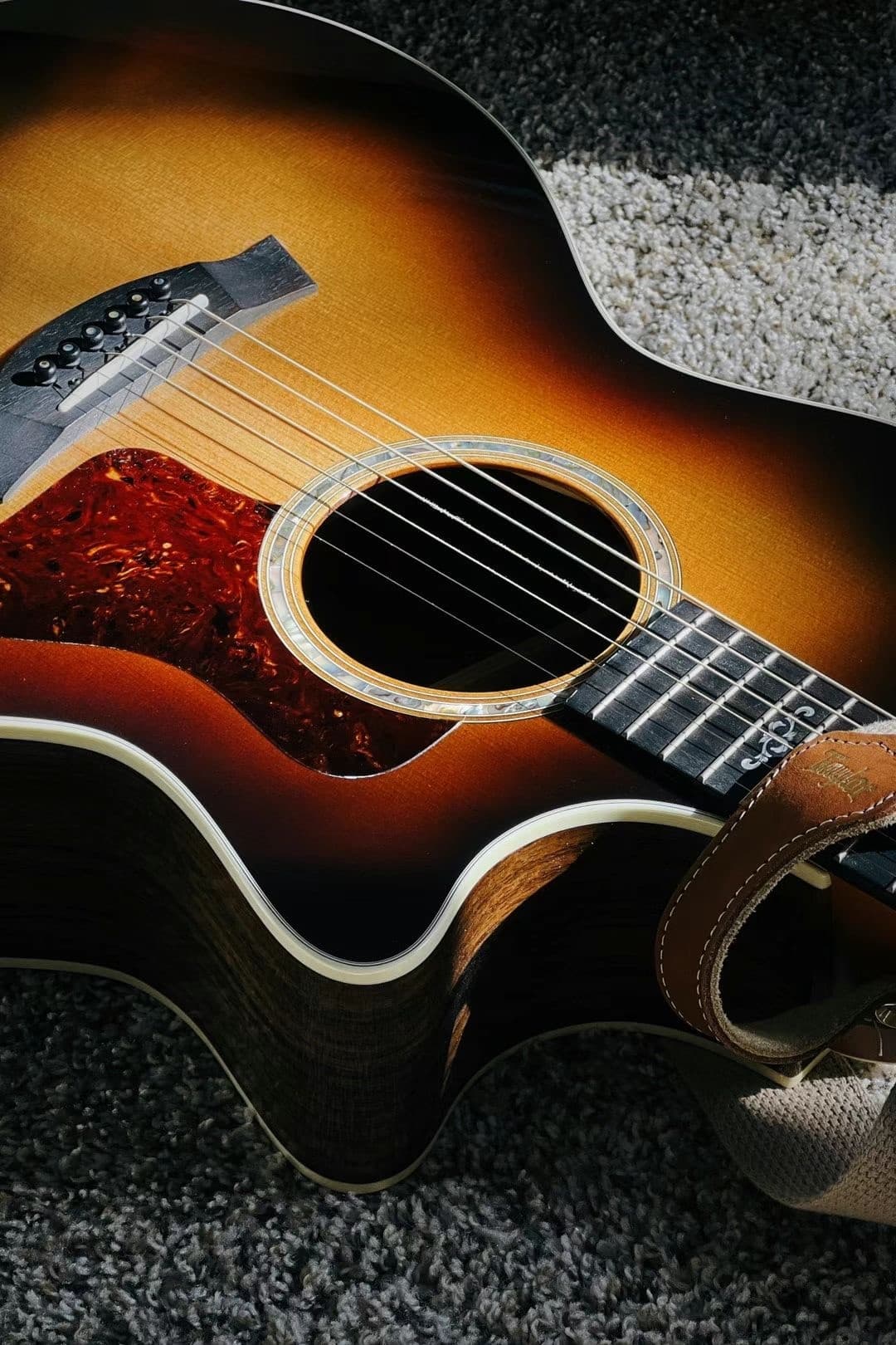 A sunburst acoustic guitar resting on a grey carpet