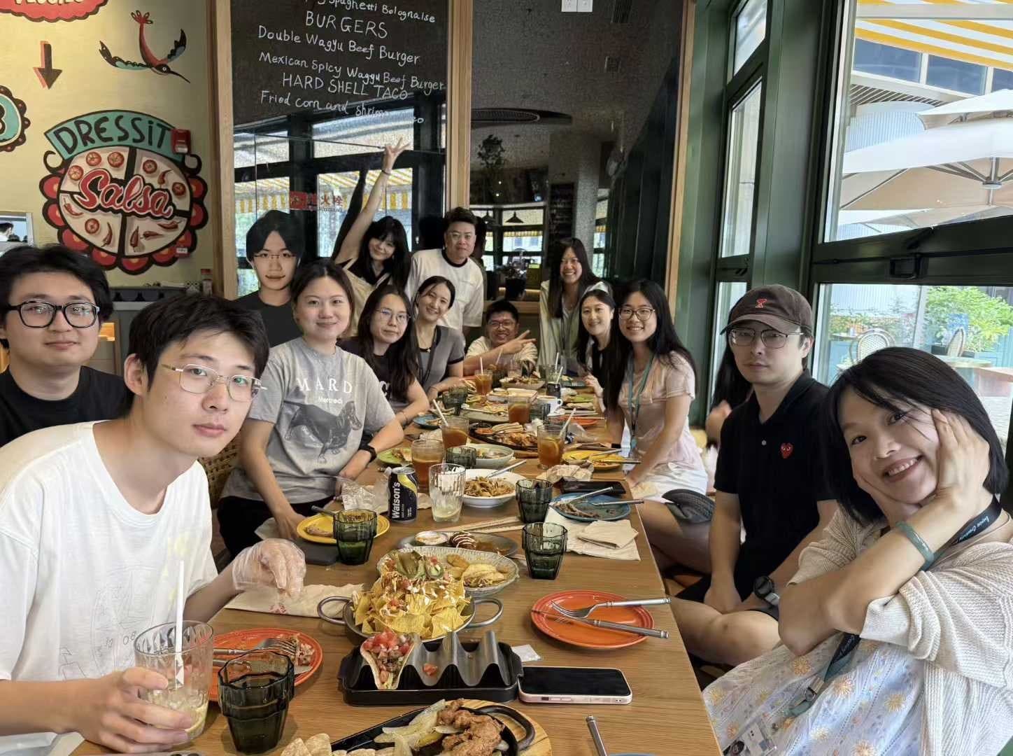 Group of friends at a restaurant table with burgers, salsa decorations on the wall