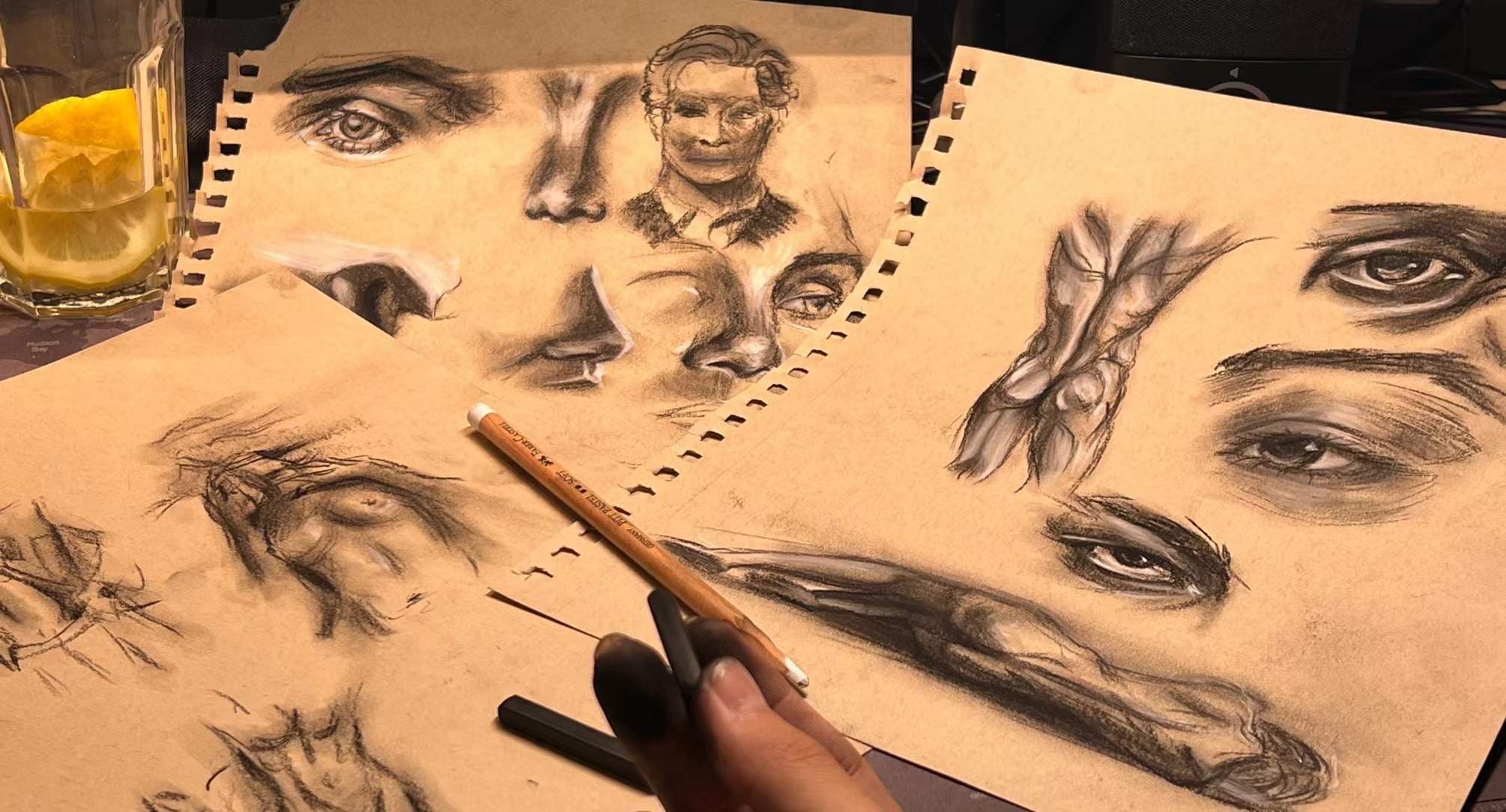 Multiple charcoal sketches of faces and hands on cream paper