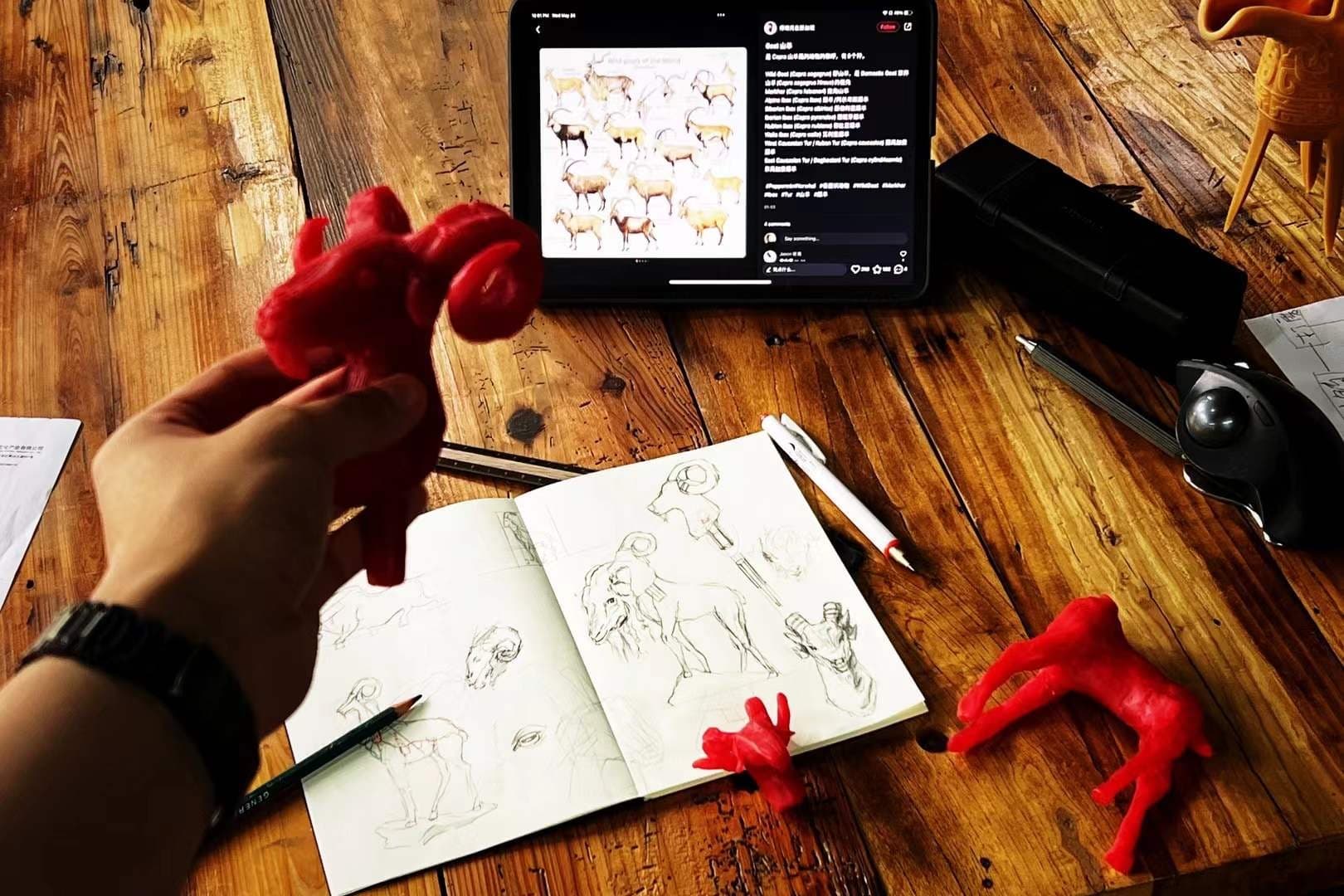 Wooden desk with iPad of horse-anatomy refs, sketchbook drawings, red sculpted clay animals