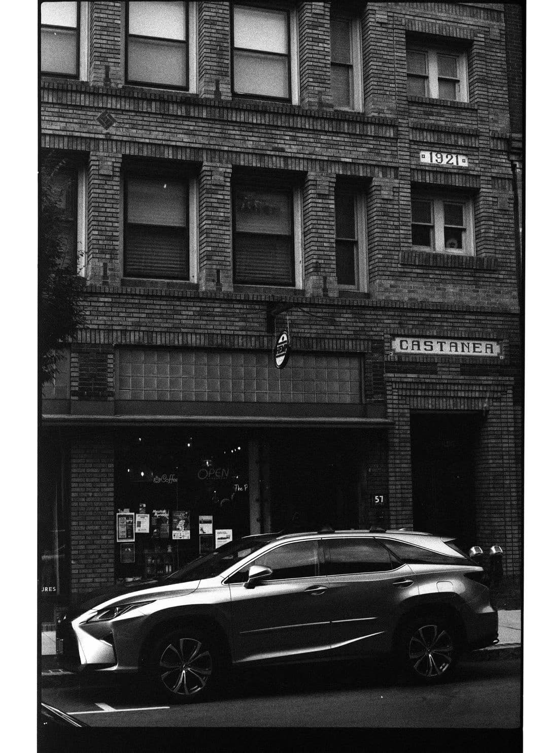 Black-and-white film print of a silver SUV parked in front of an old brick building