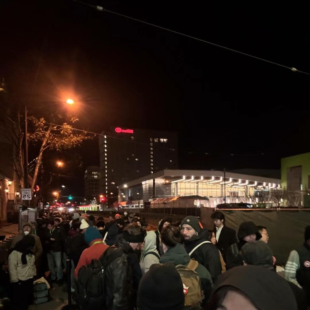 Crowd of attendees in winter coats lined up at night outside a convention center