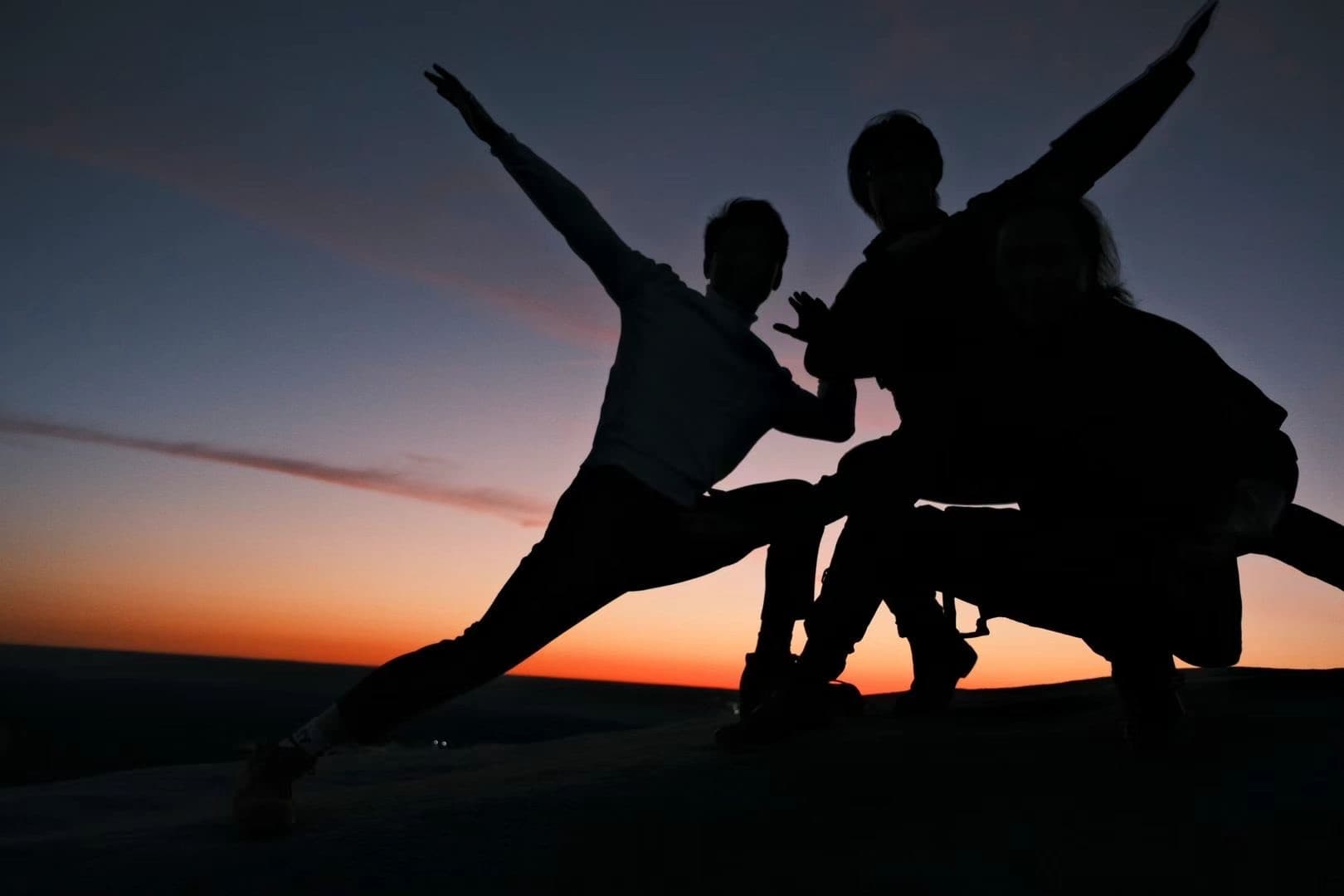 Three friends in silhouette jumping against a sunset sky